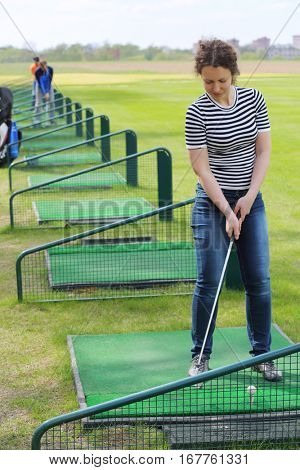 Young woman stands with cammock prepares for hit in green golf course, two men out of focus