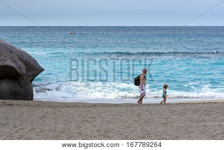ADEJE, TENERIFE, SPAIN - DECEMBER 2015: Father and daughter are walking along sandy beach of Adeje town on Tenerife isla
