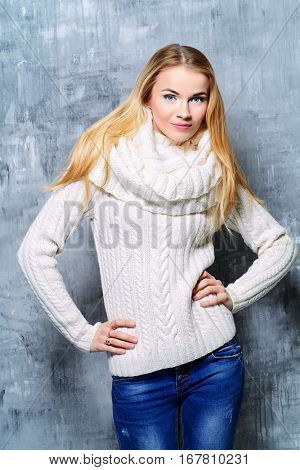 Winter beauty, cosmetics. Beautiful blonde girl wearing white sweater and a snood smiling at camera. Winter fashion concept.