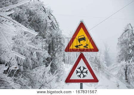 Dangerous and icy road sign with sleet covered trees. Danger on the road black ice danger wintertime concept.