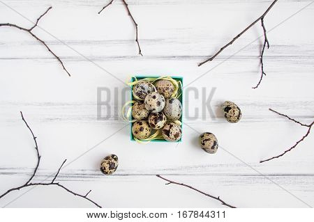 Easter floral background quail eggs in a bright blue box decorated with yellow raffia ribbon and tree branches on vintage wooden table. Flat lay top view view from above