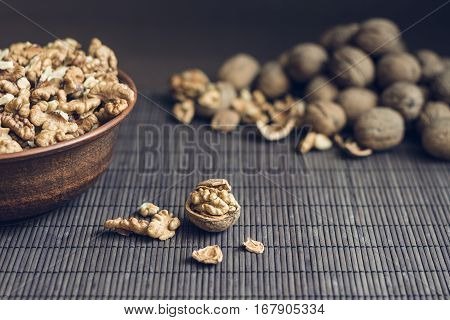 Walnut kernels and whole walnuts in brown ceramic bowl. Healthy organic food concept. Small debth of field