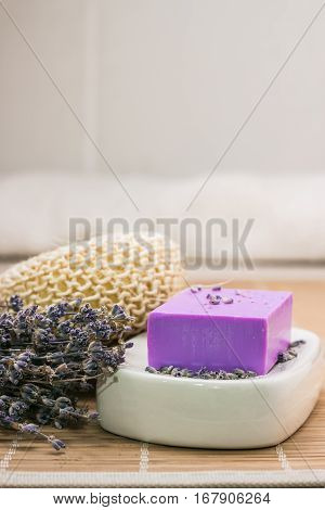 Bar of natural lavender soap on white ceramic soap dish over beige bamboo mat background
