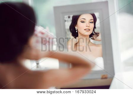 Portrait of young beautiful bride preparing to her wedding day. Gorgeous woman looking at mirror at her make-up and hairstyle