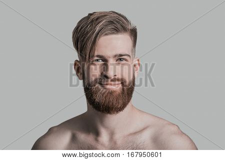 Smiling handsome. Portrait of handsome man looking at camera and smiling while standing against grey background