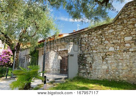 Beautiful Street Of Toscolano-maderno Town In Italy. Old Wall Made Of Stone Surrounded By Olive Tree