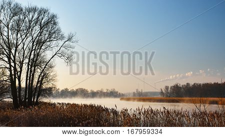Mist rising from the river in the morning. The smoke from the chimney on blue sky.