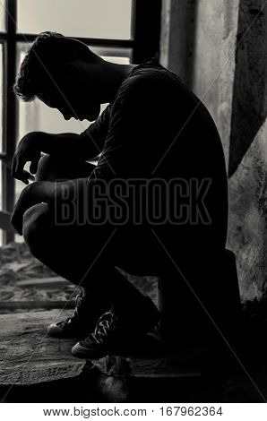 Profile of man silhouetted by a window with his head bowed and his hands, vertical shot