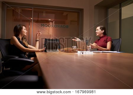 Two businesswomen working late in an office talking
