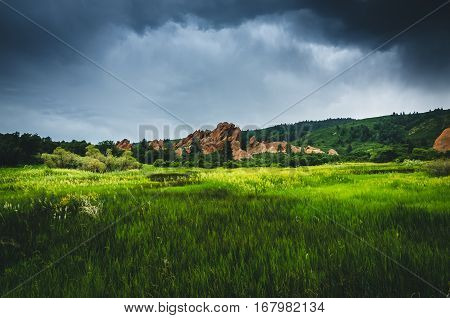 Landscape of a green field with rock formations before a storm.