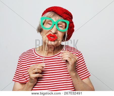 lifestyle, people and party concept: funny grandmother wearing red clothes holding falce glasses
