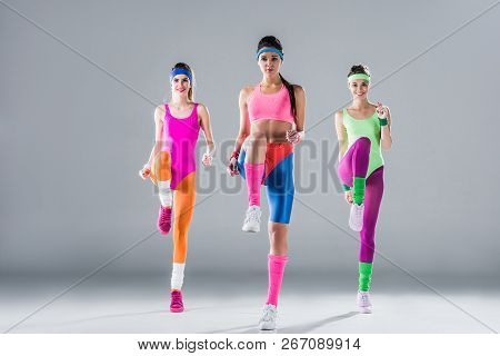 Happy Sporty Girls In Bodysuits Training At Aerobics Workout On Grey
