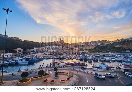 Ghajnsielem, Malta - June 15, 2018: The Waters Of Mgarr Harbour Reflect The Bright Fiery Sunset And 