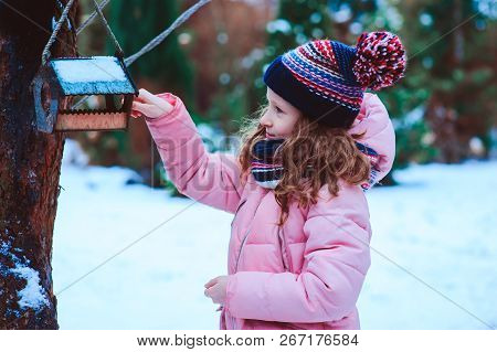 Child Girl Feeding Birds In Winter. Bird Feeder In Snowy Garden, Helping Birds During Cold Season, T