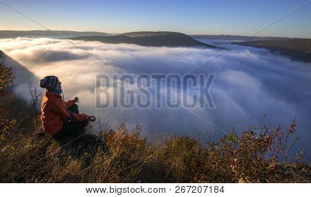 Woman Dressed In Orange Jacket Has Is Meditating Over Beautiful Landscape. Woman Is Seating Between 