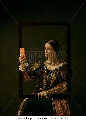 Portrait Of A Girl Wearing A Princess Or Countess Dress With Mobile Phone Over Dark Studio Making Se