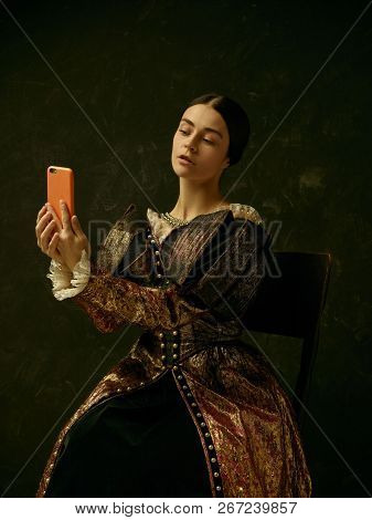 Portrait Of A Girl Wearing A Princess Or Countess Dress With Mobile Phone Over Dark Studio Making Se