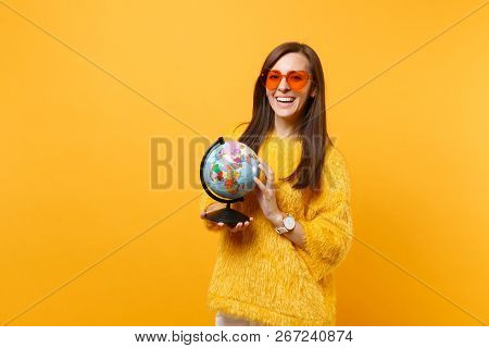 Portrait Of Smiling Happy Young Woman In Fur Sweater And Orange Heart Glasses Holding World Globe Is