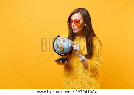 Portrait Of Curious Pretty Young Woman In Fur Sweater, Orange Heart Glasses Looking On World Globe I