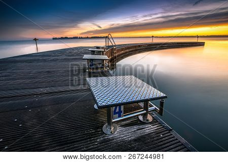 Beautiful Morning At The Lake On A Long Jetty With Wooden Planks, Morning Dew And A Colorful Sunrise