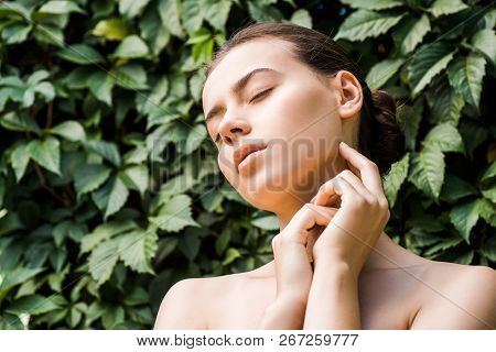 Young Woman With Hands Near Face On Green Leaves Background