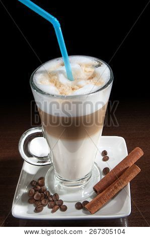 Latte Macchiato In A Glass With White Plate, Spoon, Decorated With Coffee Beans, Cinnamon On Black B