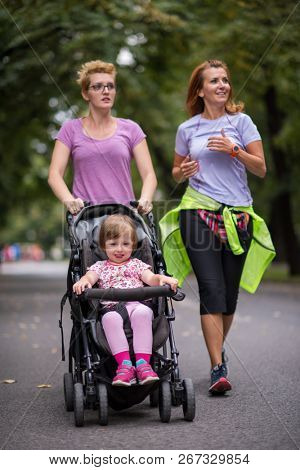 two young healthy women jogging together while pushing a baby stroller at city park
