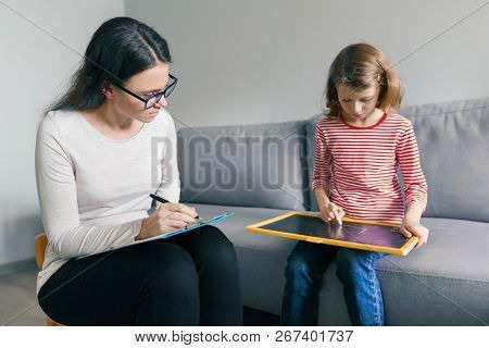 Professional Child Psychologist Talking With Child Girl In Office, Child Draws A Drawing.