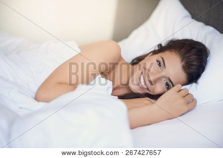 Young Beautiful Latin Woman Woman With Long Brunette Hair Lying In Her Bed With White Sheets Smiling