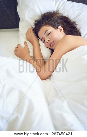 Young Beautiful Latin Woman Woman With Long Brunette Hair Lying In Her Bed With White Sheets Smiling
