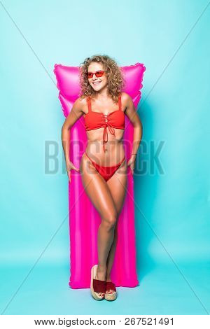 Full Length Portrait Of A Young Curlu Woman In Red Bikini Holding A Swimming Pink Mattress Against G