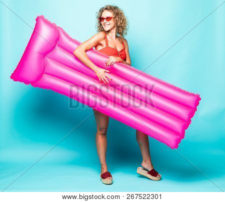 Full Length Portrait Of A Young Curlu Woman In Red Bikini Holding A Swimming Pink Mattress Against G