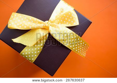 Brown Gift Box With Yellow Ribbon On Orange Background. Top View With Copy Space.