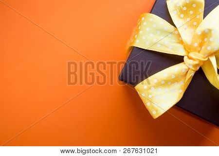 Brown Gift Box With Yellow Ribbon On Orange Background. Top View With Copy Space.