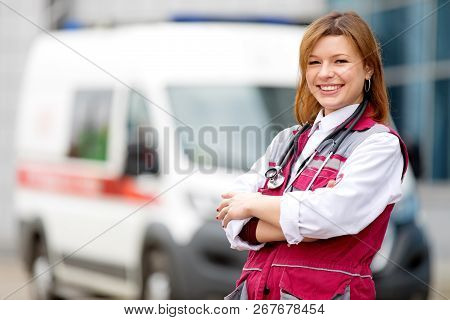 Medical Concept. Happy Paramedic Female With Phonendoscope At Emergency Car Background