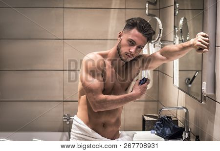 Young Man In Bathroom, Spraying Deodorant On Armpits