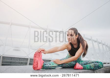Quiet And Concentrated Young Woman Stratches Her Body. She Leans To One Leg. Model Working Outside A