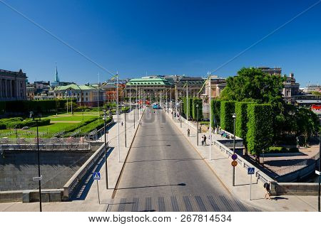 Top View From Royal Palace Of Riksplan Green Lawn And Bushes And Street With National Flags On Soder