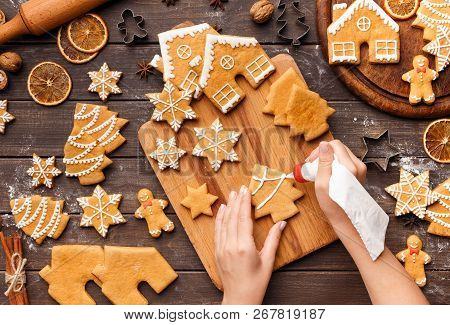 Woman Decorating Homemade Gingerbread Cookies With Royal Icing On Wooden Table, Top View