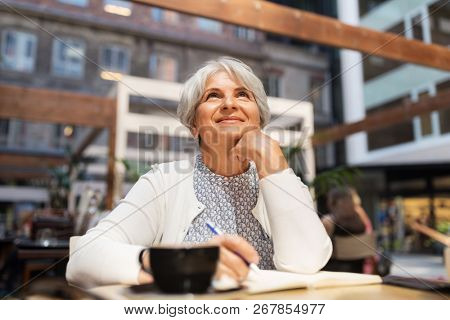 old age, leisure, retirement and people concept - happy senior woman with coffee and notebook dreaming at street cafe
