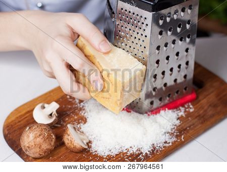 Preparation Of Baked Eggs With Mushrooms. Female Hands Grating Parmesan Cheese On Fine Grater
