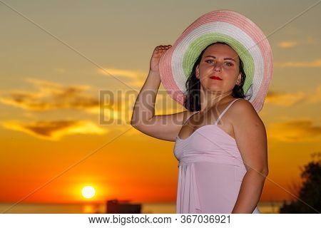 Woman In A White Dress And Hat On A Background Of A Sunset Sky.