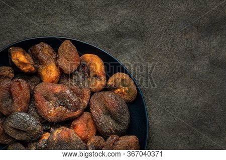 sun dried apricots - fruits on a black plate against textured bark paper with a copy spce