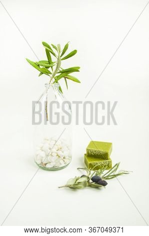 An Olive Branch In A Vintage Glass Bottle On White Wall Background And A Handmade Olive Soap Bar.