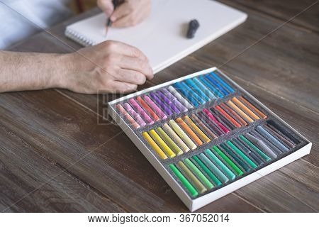 Artist Painting With A Pastel Crayon Chalk On A White Sheet Of Paper With Pallette Of Pastel Chalks 