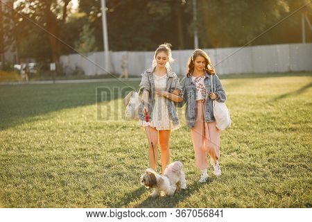 Two Girls Wallking In A Park With A Little Dog