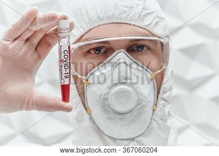COVID-19. Doctor, microbiologist, scientist in a protective suit, shows test tube with blood sample of an infected person on a white background. Coronavirus test.