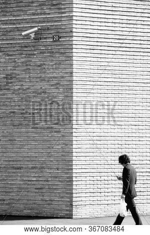 Cctv Camera On A Brick Wall And A Man Walking By