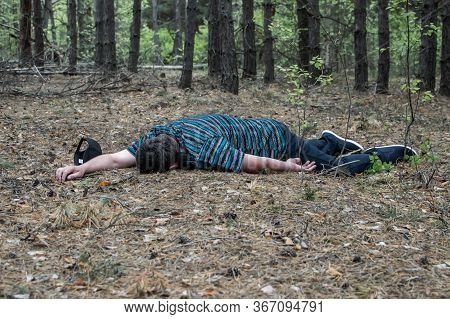 Murder In The Woods. The Body Of A Man In A Blue T-shirt And Trousers Lies On The Ground Among The T