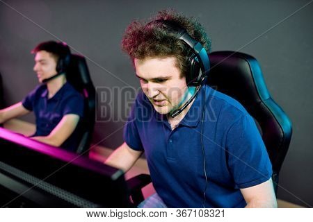 Young operator of e-sport call center in headset looking at computer screen while commenting network game with tense expression